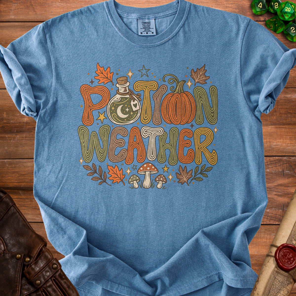 Blue t-shirt with "Potion Weather" text, potion bottle, pumpkin, and mushrooms.