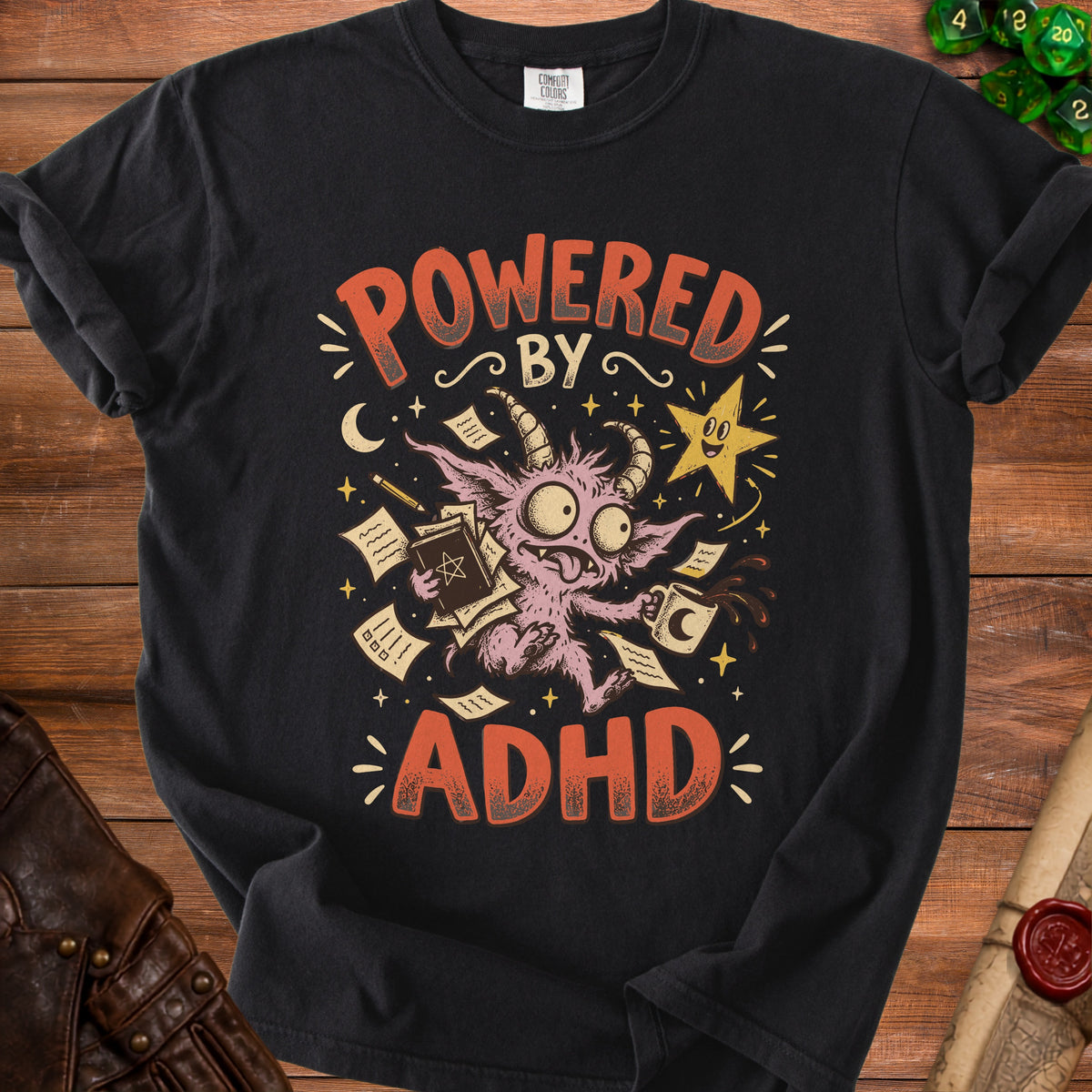 Black t-shirt with cartoon creature, coffee, books, and text "POWERED BY ADHD".