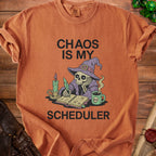 Orange t-shirt with skeleton wizard graphic reading "CHAOS IS MY SCHEDULER".
