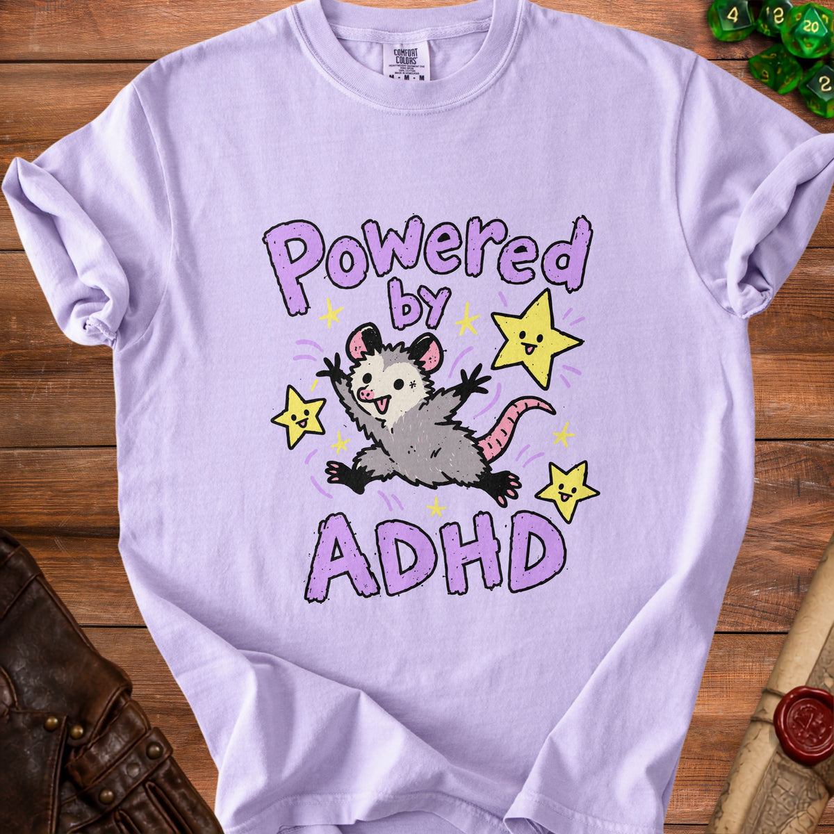 Light purple t-shirt with a cartoon possum and stars, reading "Powered by ADHD."