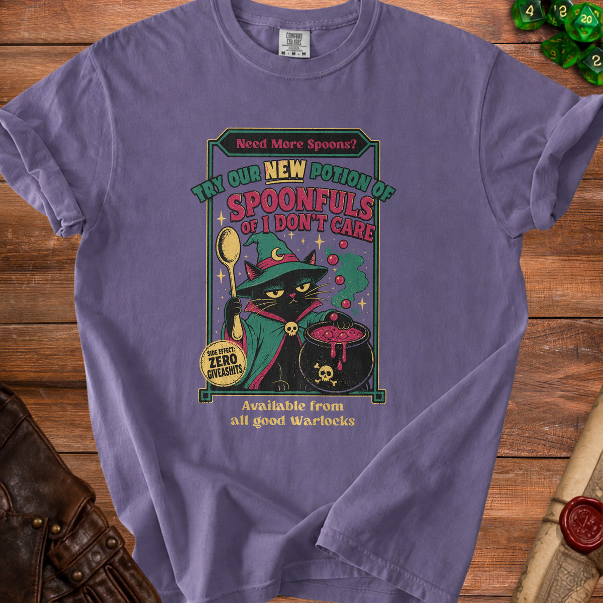 Purple t-shirt graphic with a black cat holding a spoon, wearing a witch hat, and a cauldron. Text says "Need More Spoons? Try Our New Potion of Spoonfuls of I Don't Care."