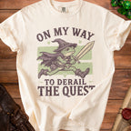Cream t-shirt with frog wearing a wizard hat, cape, and boots, holding a sword, with text "ON MY WAY TO DERAIL THE QUEST".