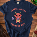 Dark blue t-shirt with a cartoon demon holding a pentagram mug, reading "Please Summon Someone Else".