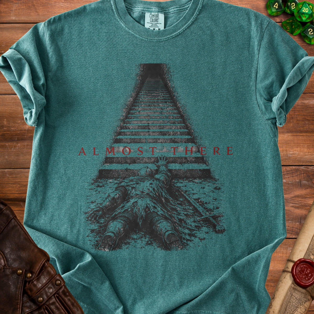 Green t-shirt with dark print of fallen knight and stairs, text "ALMOST THERE."