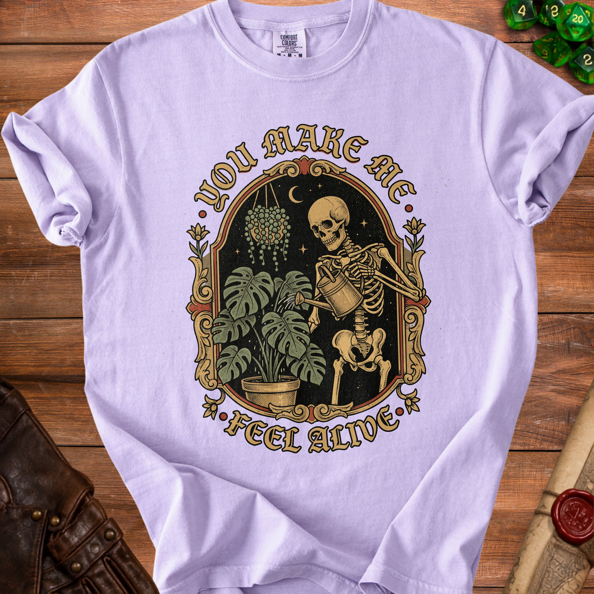 Skeleton watering plants with text "YOU MAKE ME FEEL ALIVE" on purple shirt.