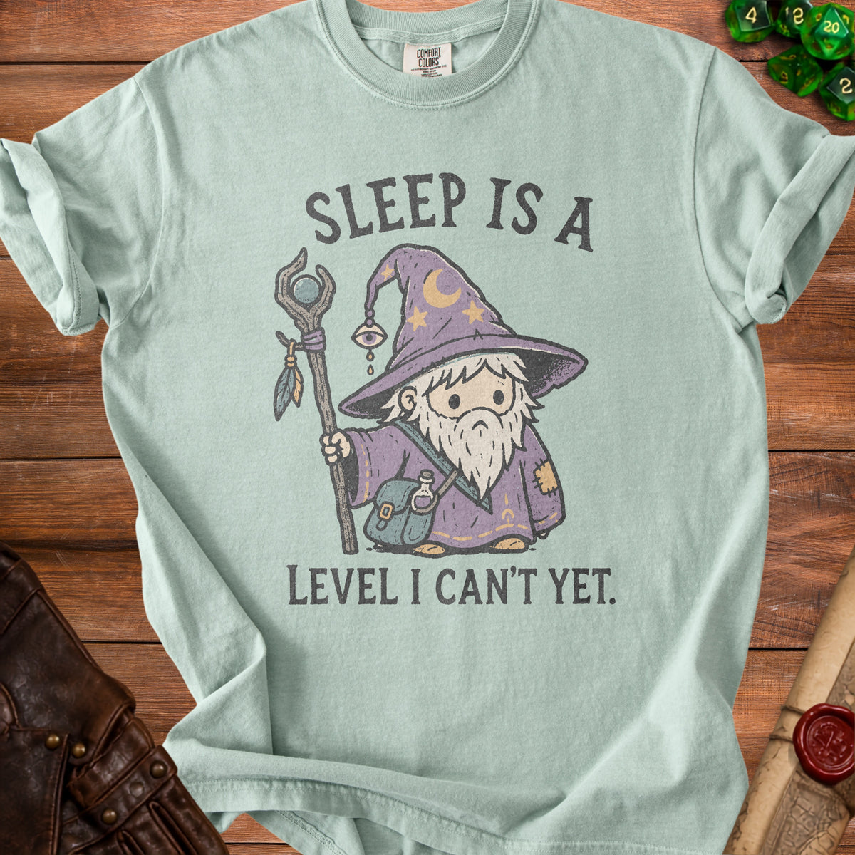 Light teal t-shirt with a cartoon wizard and text "SLEEP IS A LEVEL I CAN'T YET."