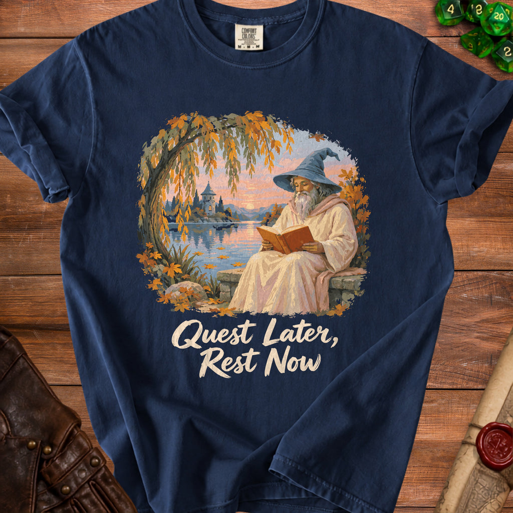 Dark blue t-shirt with a wizard reading a book by a lake and the text "Quest Later, Rest Now".