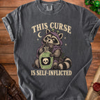 Dark gray t-shirt with raccoon graphic and text "THIS CURSE IS SELF-INFLICTED".