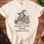 Skeleton wizard writing with quill at desk with letters and "Dragon Slain, Inbox Undefeated" text.