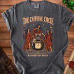 Dark grey t-shirt graphic with three witches around a potion bottle, text "THE CAFFEINE CIRCLE RESTORE THE PARTY".