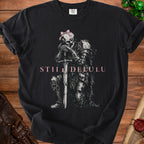 Black t-shirt with skeleton knight graphic, pink bow, and "STILL DELULU" text.