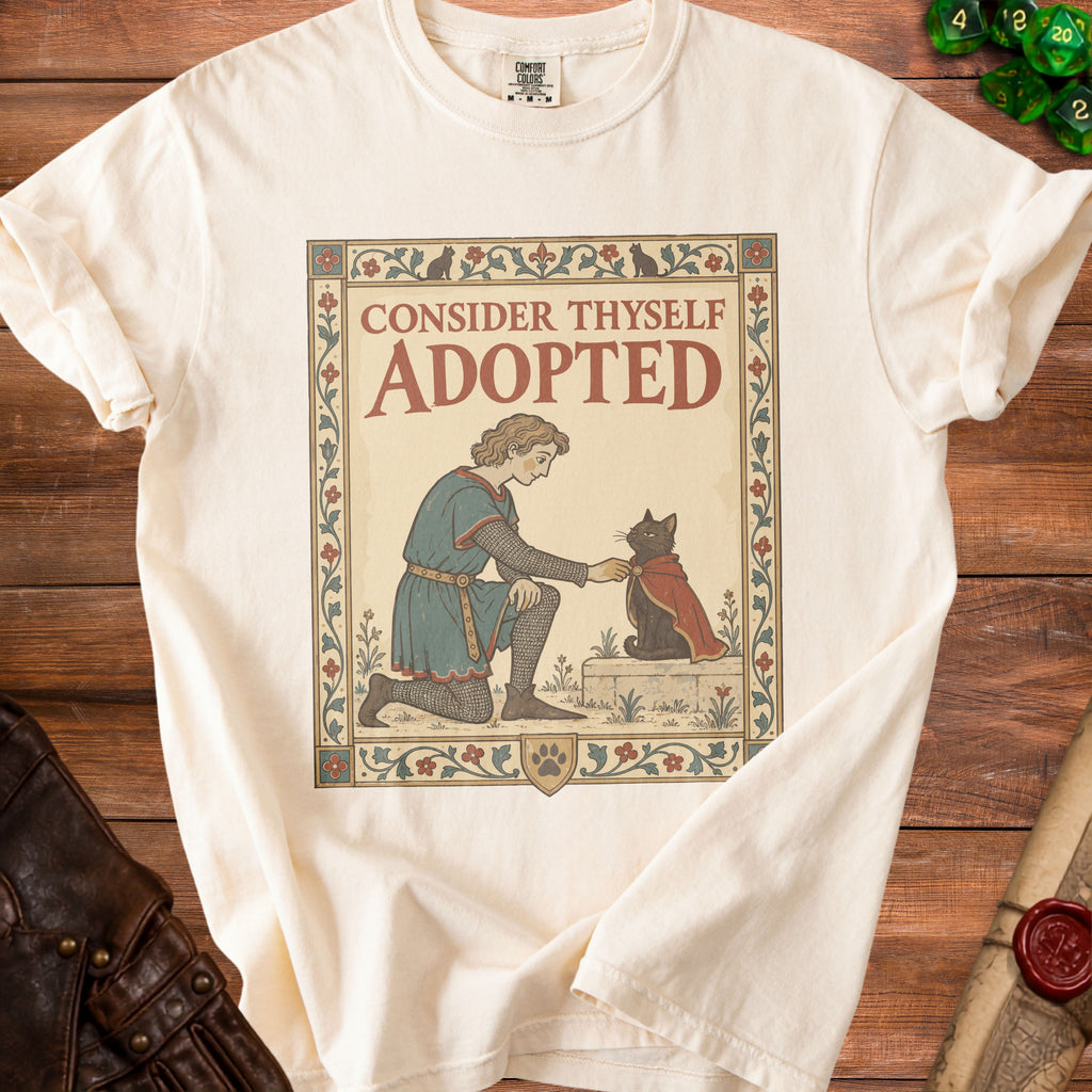 Cream t-shirt with medieval-style art of a person offering a cape to a black cat.
