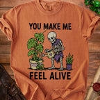 Skeleton watering plants with text "YOU MAKE ME FEEL ALIVE".