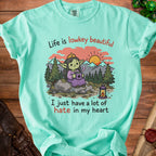 T-shirt with graphic of goblin drinking coffee, text "Life is lowkey beautiful, I just have a lot of hate in my heart."