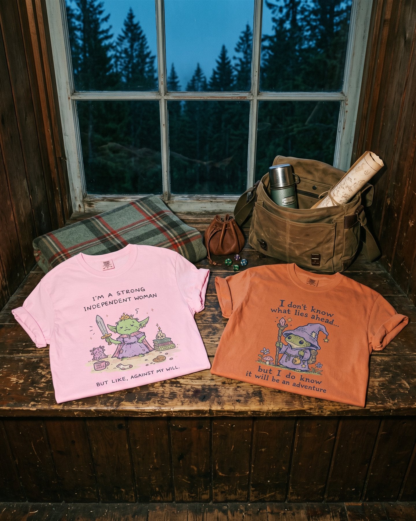 The Against My Will and Frog Wizard adventure tees laid out beside a packed satchel with dice and snacks